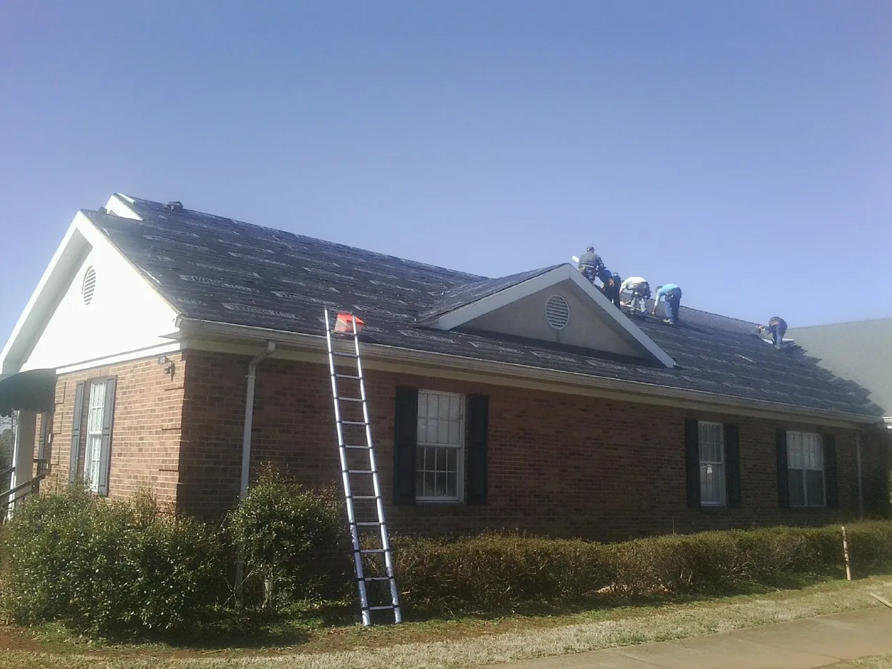Crew tearing shingles off a brick ranch roof with a ladder set — Metal Roof Repair work by our crew in Limekiln