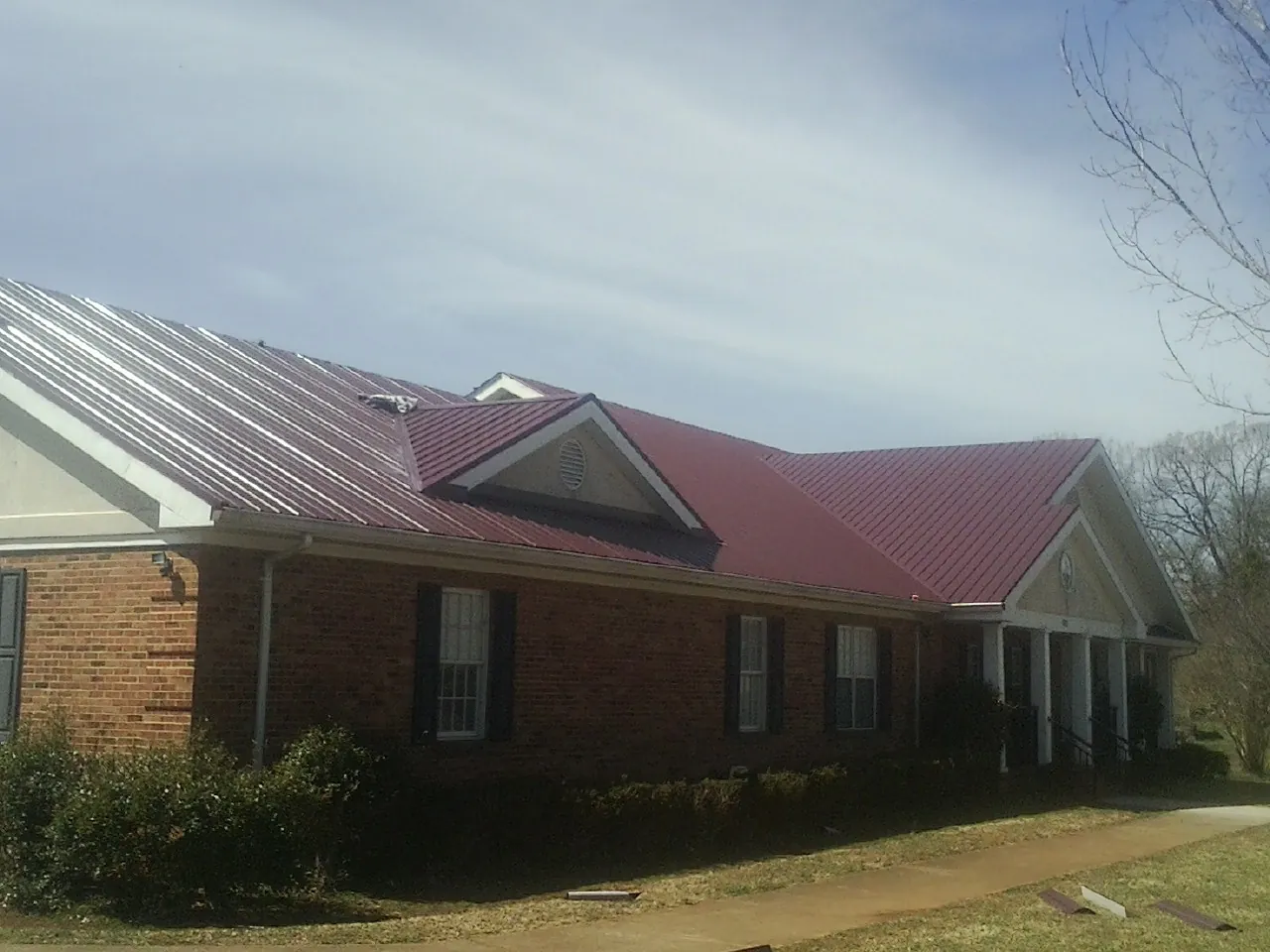 Red metal roof with gabled entries on a long brick building, from a Hail Damage Roof Repair job in Limekiln