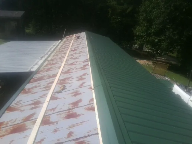 Old rusted panels beside newly installed green metal roofing — Wind Damage Roof Repair by Roofing Brothers in Limekiln