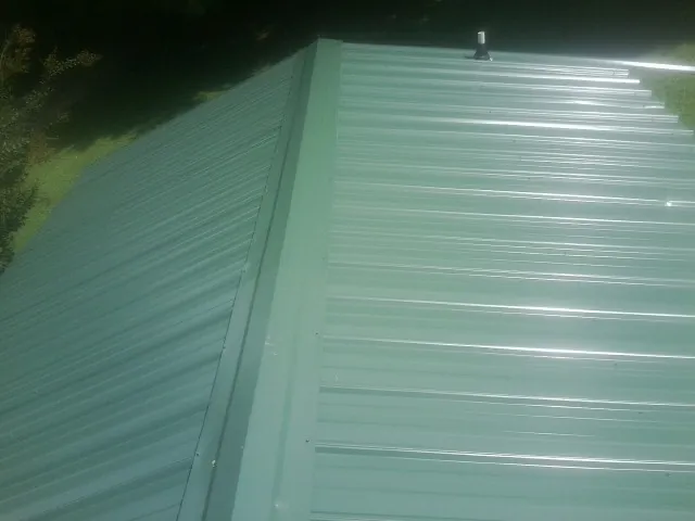 New green metal panels meeting at the ridge of a roof — Flat Roof Repair work by our crew in Limekiln
