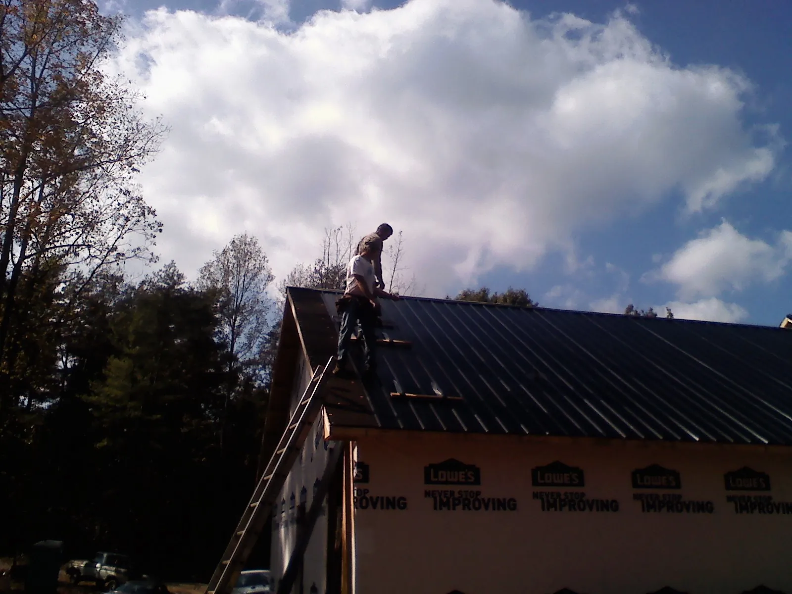 Roofer fastening dark metal panels high against a cloudy sky, from a Roof Inspection job in Limekiln