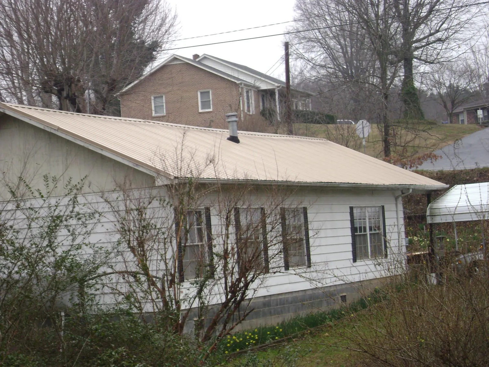 Tan metal roof on a white sided house set into a hillside — Commercial Roofing by Roofing Brothers in Limekiln